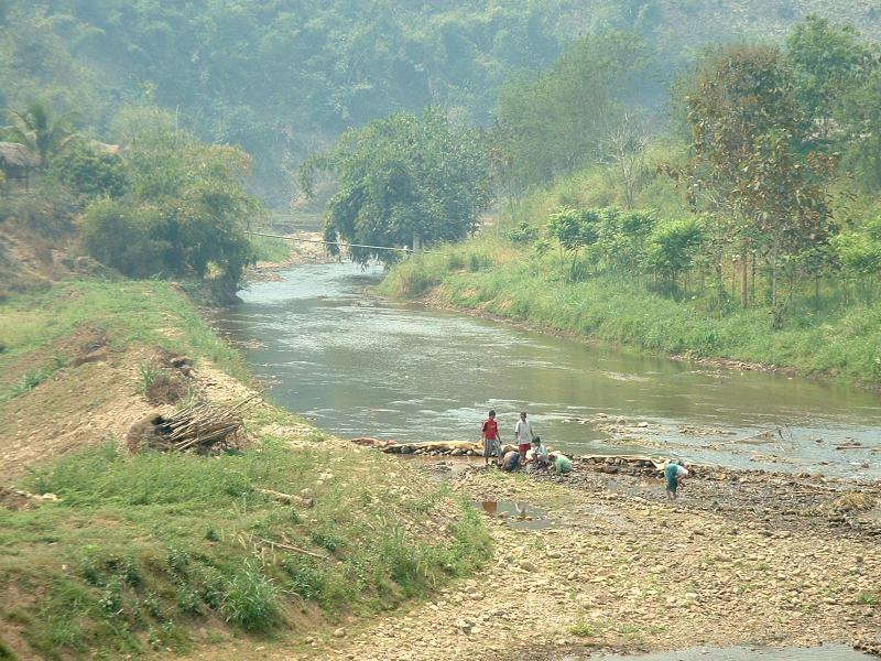 Les enfants jouent au bord de l'eau pendant que les adultesramassent des crustacés (?)